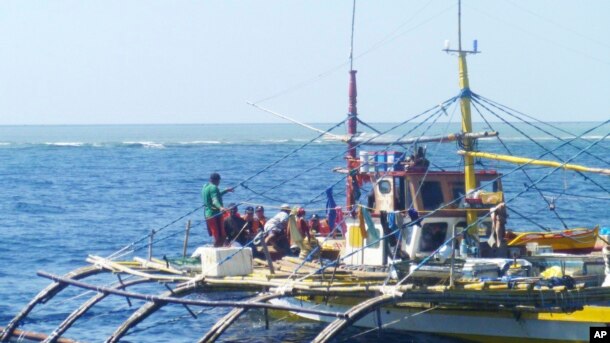 In this photo provided by Renato Etac, Chinese Coast Guard members, wearing black caps and orange life vests, approach Filipino fishermen as they confront them off Scarborough Shoal at South China Sea in northwestern Philippines, Sept. 23, 2015.