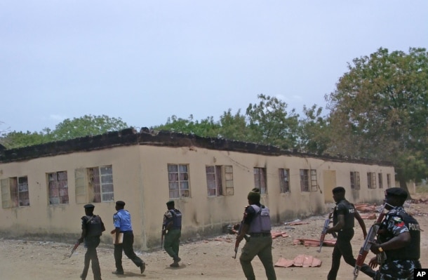 FILE - Security guards walk past a burned-out government secondary school in Chibok, Nigeria. April, 21. 2014.