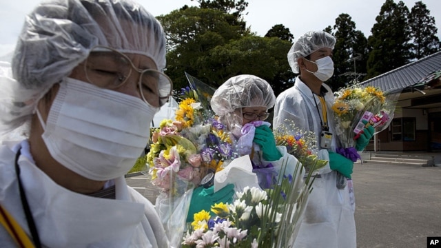 Mourners in protective suits hold flowers at memorial for residents of Okuma, a small town near Fukushima Dai-Ichi nuclear power plant, Japan, July 2011.