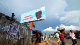People walk past a campaign poster for incumbent President Ernest Bai Koroma, in Freetown, Sierra Leone, Oct. 19, 2012. 