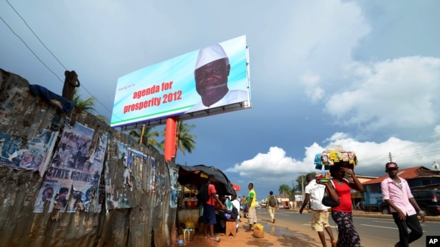 People walk past a campaign poster for incumbent President Ernest Bai Koroma, in Freetown, Sierra Leone, Oct. 19, 2012. 