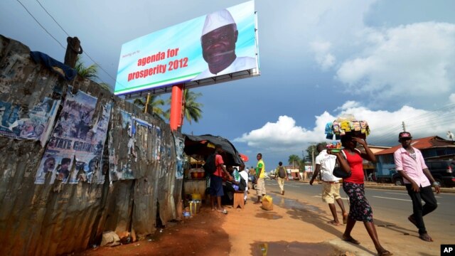 People walk past a campaign poster for incumbent President Ernest Bai Koroma, in Freetown, Sierra Leone, October 19, 2012. 
