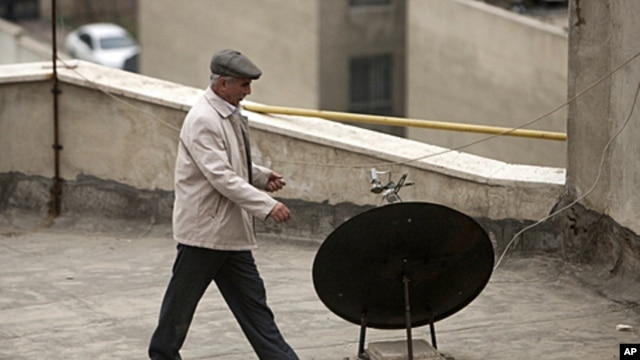 An Iranian man walks past a satellite dish on a rooftop in northern Tehran, January 15, 2011.