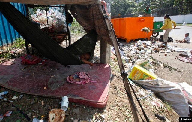 A young girl sleeps in a hammock as her mother clears garbage, along a street in central Phnom Penh October 3, 2014. REUTERS/Samrang Pring