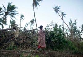 A woman carrying her baby walks past fallen trees on the southern island of Tanna, where residents told relief workers they were running low on food and other basic supplies, March 18, 2015.