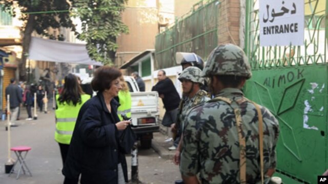 A woman enters a polling station guarded by soldiers and police during the first round of Egypt's run-off parliamentary elections in Cairo, December 5, 2011.