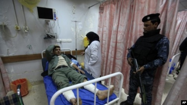 A police officer stands guard near his wounded comrade after a bomb attack, at a hospital in Baghdad, February 19, 2012.