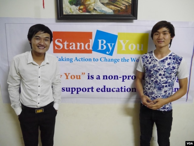 Phạm Minh Dap (trái) và em trai đứng trước một tấm băng rôn quảng cáo lớp học ngoại ngữ miễn phí Stand By You cho học sinh, sinh viên nghèo (Marianne Brown/VOA)