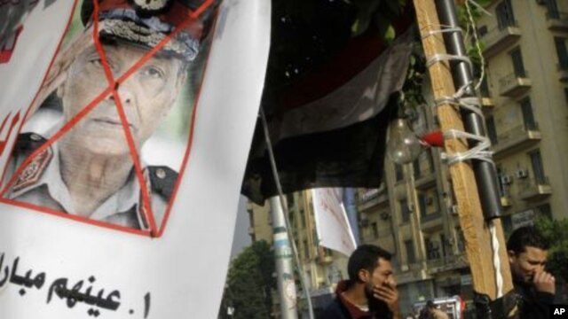 Protesters walk next to a poster against Egypt's military ruler, Field Marshal Mohamed Hussein Tantawi, the head of the Supreme Council of the Armed Forces, at Tahrir Square, the focal point of Egyptian uprising, in Cairo, Egypt, November  27, 2011.