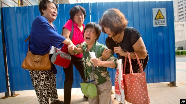 Bao Lanfang, second from right, whose daughter-in-law, son and granddaughter were aboard Malaysia Airlines Flight 370, kneels in grief while speaking to journalists outside the company's offices in Beijing, Aug. 6, 2015.  