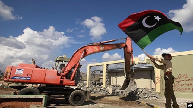 A boy waves a Kingdom of Libya flag as a bulldozer demolishes walls of the residence of Moammar Gadhafi at the Bab al-Aziziyah complex in Tripoli, October 16, 2011.