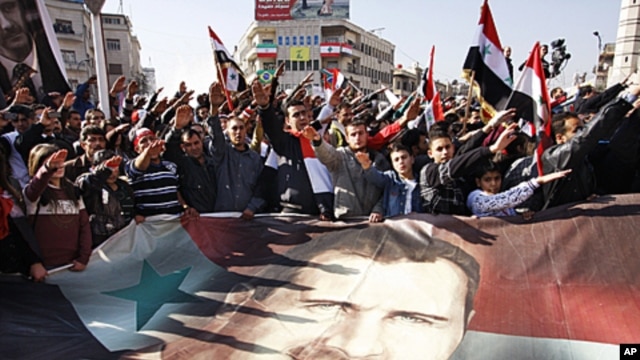 Syrians hold a large poster depicting Syria's President Bashar Assad during a rally in Damascus, Syria. Syria signed an Arab League initiative Monday that will allow Arab observers into the country as part of peace deal that aims to end the nation's incre
