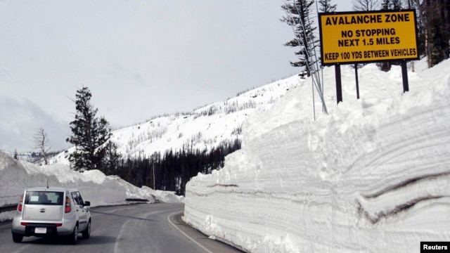 FILE - A car travels the newly plowed east entrance road over Sylvan Pass in Yellowstone National Park shortly after the park opened in this photo taken in May 2011.