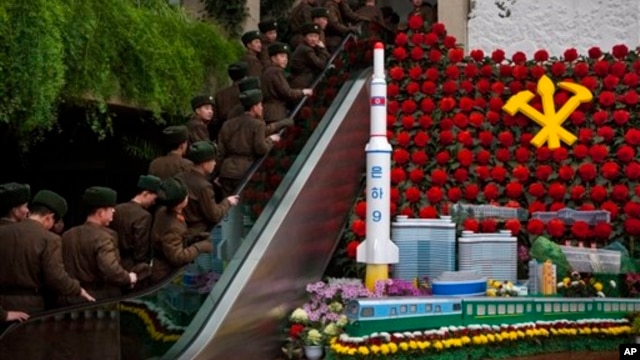 North Korean soldiers ride escalator past a model of the Unha Rocket alongside so-called "Kimjongilia" flowers at an exhibition in Pyongyang, Feb. 17, 2013.