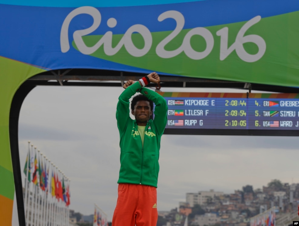 FILE - Silver medalist Feyisa Lilesa of Ethiopia crosses his writsts as he celebrates on the podium after the men's marathon at the 2016 Summer Olympics in Rio de Janeiro, Brazil, Aug. 21, 2016. He had made the same gesture of protest as he approached the finish line of the race.