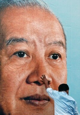 A man holds a portrait of former King Norodom Sihanouk as he and other workers try to hang it on the facade of the Royal Palace in Phnom Penh, Cambodia, as part of preparations for his funeral, October 16, 2012.