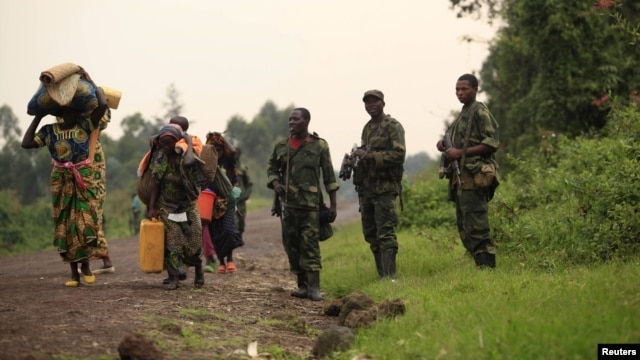 Displaced families walk past M23 rebels at Rumangabo, after government troops abandoned the town 23 km (14 miles)  north of the eastern Congolese city of Goma, July 28, 2012. 