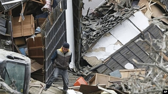 A man walks on the debris in Ishinomaki city, Miyagi prefecture after a powerful 7.1 aftershock rocked that area of Japan, April 8, 2011