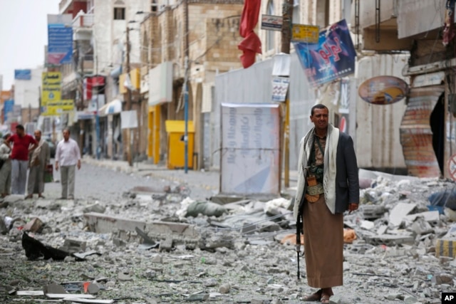 FILE - A Shiite fighter known as a Houthi stands guard in front of buildings destroyed by a Saudi-led airstrike in Sana'a, Sept. 5, 2015.