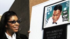 La cantante Natalie Cole observa una estampilla gigante y una placa que conmemora a su padre, el legendario Nat King Cole.