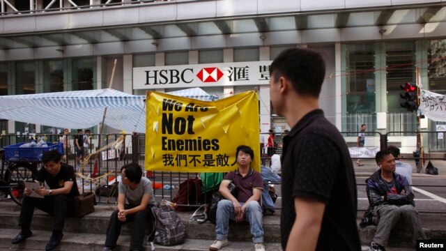 Người biểu tình ủng hộ dân chủ ngồi nghỉ dưới biểu ngữ với hàng chữ "Chúng tôi không phải là kẻ thù" bên ngoài một chi nhánh ngân hàng HSBC tại khu mua sắm Mongkok của Hồng Kông, ngày 7/10/2014.