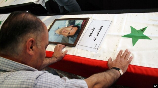 A Syrian man mourns a relative whose picture is displayed atop his coffin with Arabic words that read: "The Martyr, Atef Abdullah" during a mass funeral procession for several Syrians killed in a twin suicide bombings, at a mosque in Damascus, Syria Satur