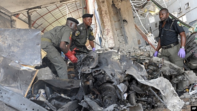 Police anti-bomb officers stand on the burnt engine of the Jeep used by the suicide bomber that ravaged ThisDay Newspapers rocked by bomb explosions killing two security men, the suicide bomber and injuring five of the company's support staff, April 26, 2