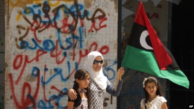 A Libyan woman holding the rebellion's flag tours with her daughters Moamer Kadhafi's destroyed headquarters of Bab al-Aziziya in Tripoli, August 31, 2011