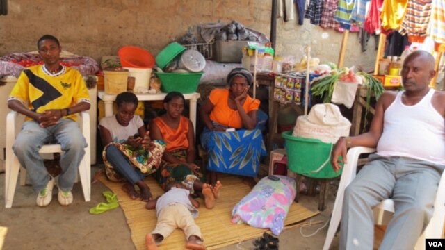 Familia de Alves Kamolingue, com a esposa sentada no chão, à esquerda e o filho no chão a dormir (VOA / Coque Mukuta)