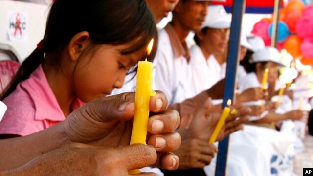 FILE - A Cambodian girl, left, HIV-positive, sits with others who are affected with HIV AIDS hold candles during a vigil in Phnom Penh, Cambodia.