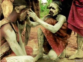 An Ogiek paints his fellow warrior's face