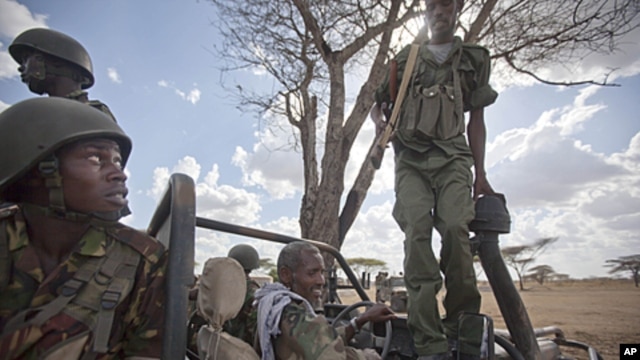 A Kenyan army soldier, left, looks up as a Somali government soldier, right, climbs across the vehicle that they are sharing, and another Somali government soldier prepares to drive, center, in Tabda, inside Somalia, February 20, 2012.