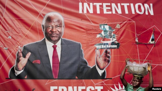 A child street vendor stands in front of a poster for Sierra Leone's ruling party presidential candidate Ernest Bai Koroma, Freetown, Nov. 16, 2012.
