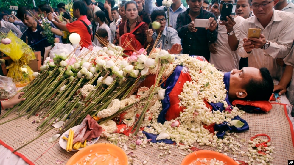 FILE - In this July 11, file photo, the body of Cambodian government critic Kem Ley is covered by the Cambodian National flag as flowers are placed during a funeral ceremony in Phnom Penh, Cambodia. Oeut Ang, the man who allegedly shot dead Kem over what 