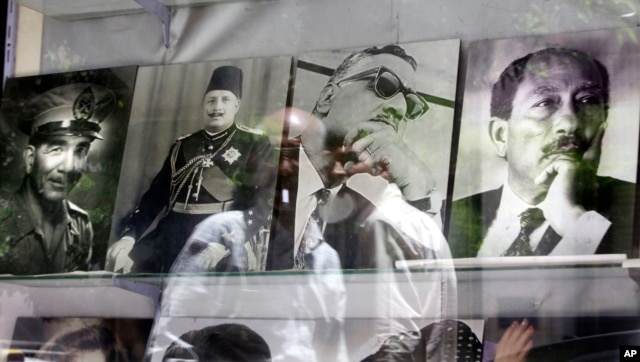 Egyptians are reflected in pictures showing late Egyptian presidents Mohammed Naguib, left, Gamal Abdel Nasser, second right, Anwar Sadat, right, and Egypt's last King Farouk, second left, at a photo shop in Cairo, Egypt, May 22, 2012.