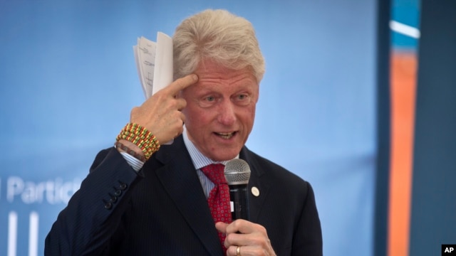 Former president Bill Clinton gestures while wearing a bracelet given to him by Kenyan students, as he and and his daughter Chelsea Clinton talk about their foundation's 