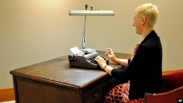 This undated photo provided by the University of South Carolina Creative Services, a woman sits at author Joseph Heller's old wooden desk and types on the battered typewriter he used to compose “Catch-22.”