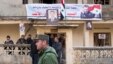 Sĩ quan cảnh sát Syria đi ngang qua nhóm người địa phương đứng tại một tòa nhà với bức chân dung Tổng thống Syria Bashar al-Assad ở Salma, Syria, ngày 22/1/2016.