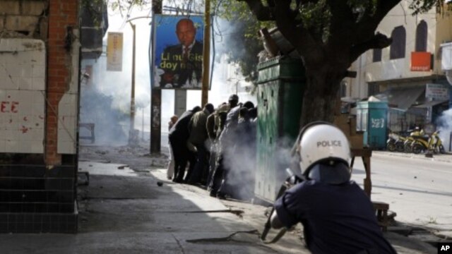 A police officer fires tear gas at close range directly into a group of anti-government protesters sheltering behind a kiosk, on a central boulevard in Dakar, Senegal, February18, 2012.
