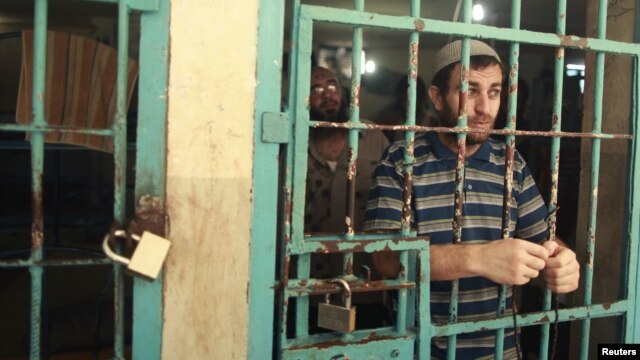A Palestinian inmate stands behind the bars of a Hamas-run jail in Gaza City after prayers during the holy month of Ramadan, July 23, 2012.