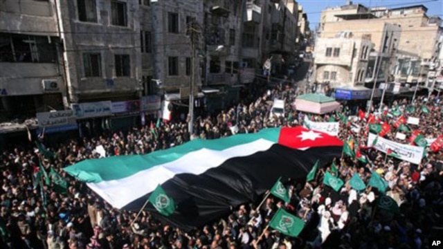 Jordanian protesters hold a giant national flag, as they march during a protest demanding the resignation of the prime minister and his government over price increases and inflation, in Amman, 21 Jan 2011