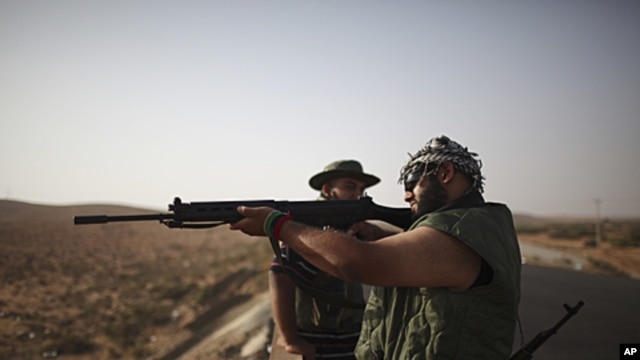 A rebel fighter checks a rifle at a checkpoint between Tarhouna and Bani Walid. Moammar Gadhafi is determined to fight his way back to power, the toppled dictator's spokesman said but a large convoy of his soldiers has apparently deserted, crossing the Li
