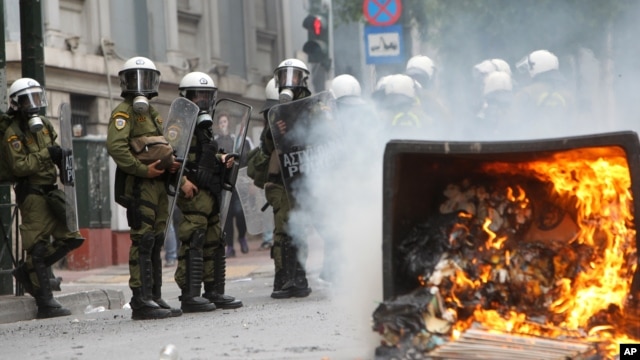 A fire burns as riot police look on during clashes with activists protesting German Chancellor Angela Merkel's visit in Athens, Greece, Oct. 9, 2012. 