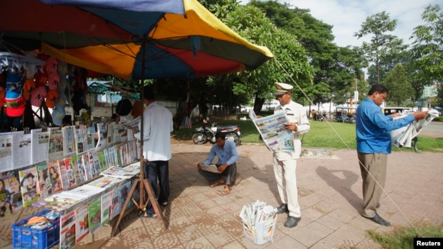 FILE - People read newspapers at a street side stand in central Phnom Penh.