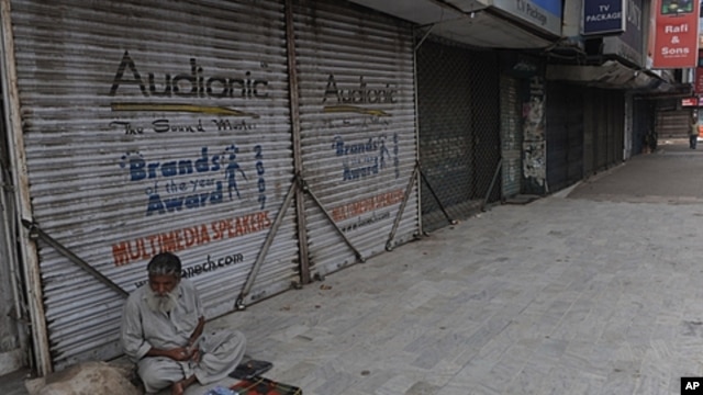 A Pakistani street vwndor sits next to a row of shuttered shops in a Karachi market after a week long period of violence in the city, March 31 2012.