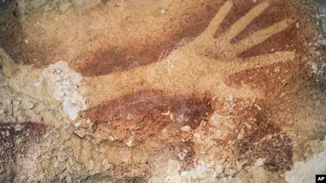 Gambar stensil tangan di gua di Sulawesi, yang menurut studi baru sama tuanya dengan seni prasejarah di Eropa. (AP/Kinez Riza, Nature Magazine)