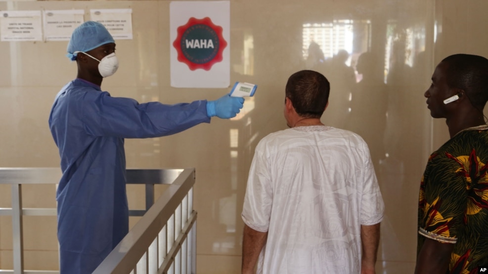 FILE - A health worker, center, takes the temperature of people to see if they might be infected by the Ebola virus inside the Ignace Deen government hospital in Conakry, Guinea, March 18, 2016.