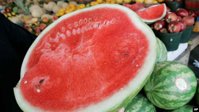 A person holds a cut watermelon at a fruit stand. 