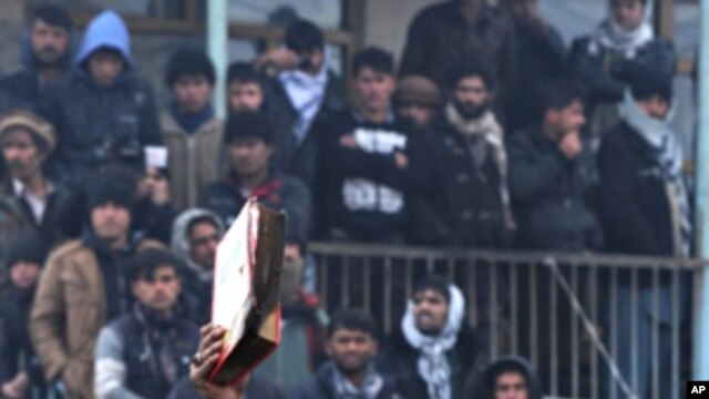 An Afghan demonstrator holds a copy of a half-burnt Quran, allegedly set on fire by US soldiers, at the gate of Bagram airbase during a protest against Koran desecration at Bagram, about 60 kilometers (40 miles) north of Kabul, February 21, 2012.