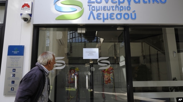 An elderly man holds his bank passbook as he looks through the windows of a closed cooperative bank shop in Limassol, Cyprus,  Mar. 16, 2013.